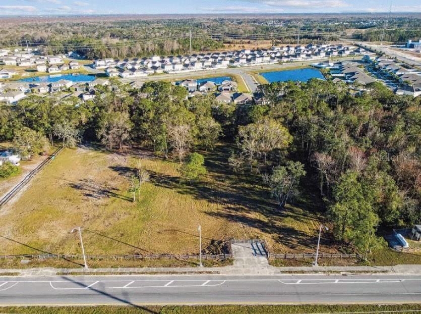 An aerial view of a vacant, grassy lot bordered by trees and a residential neighborhood — 6020 US HIGHWAY 17 92 N, DAVENPORT, FL