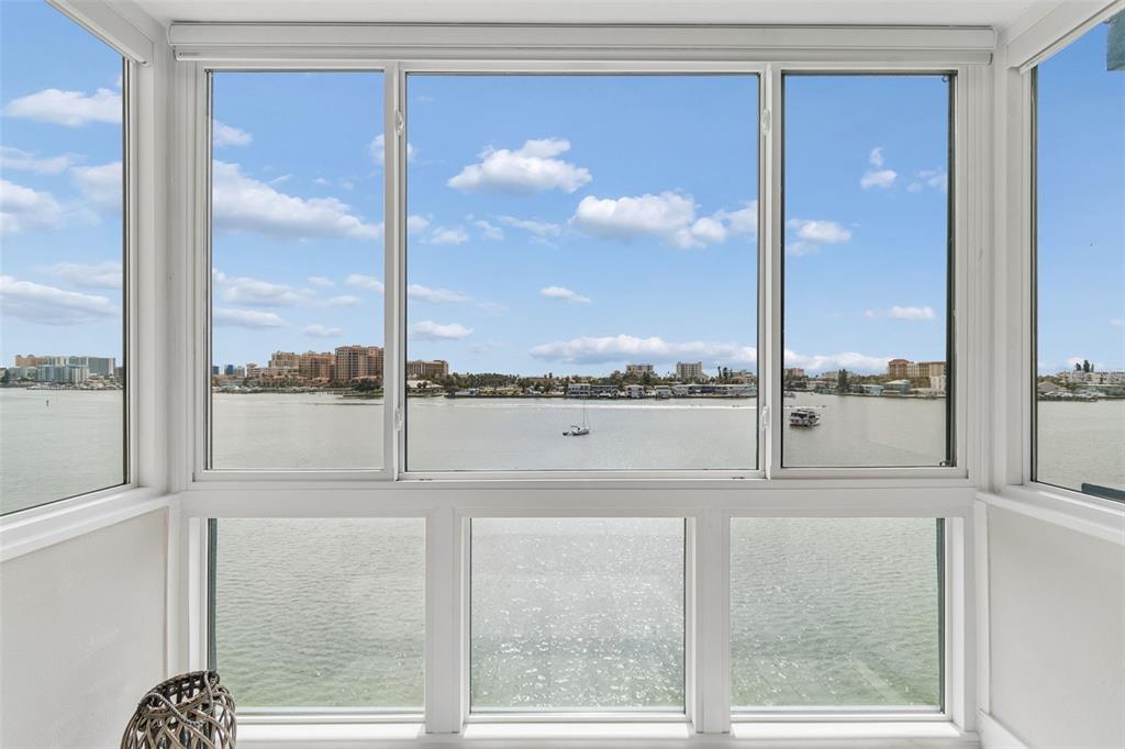 A sunroom with large windows overlooking a bay, distant buildings, and a boat — 644 ISLAND WAY UNIT 603, CLEARWATER BEACH, FL