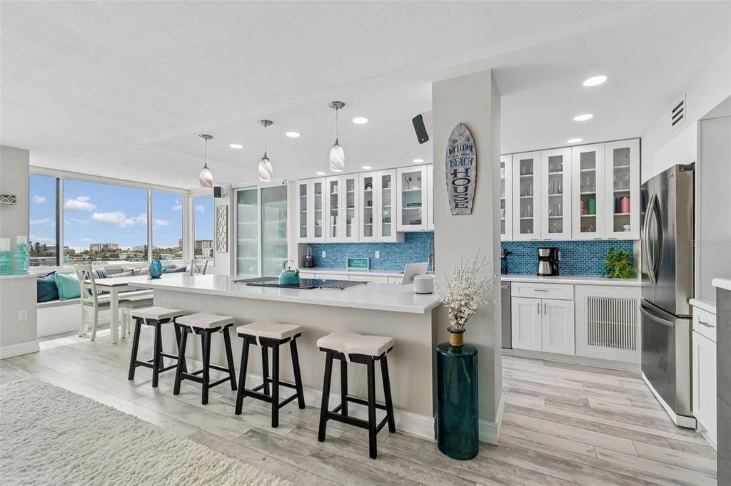 A bright kitchen features white cabinetry, a quartz island with bar seating, and blue tile backsplashes — 644 ISLAND WAY UNIT 603, CLEARWATER BEACH, FL