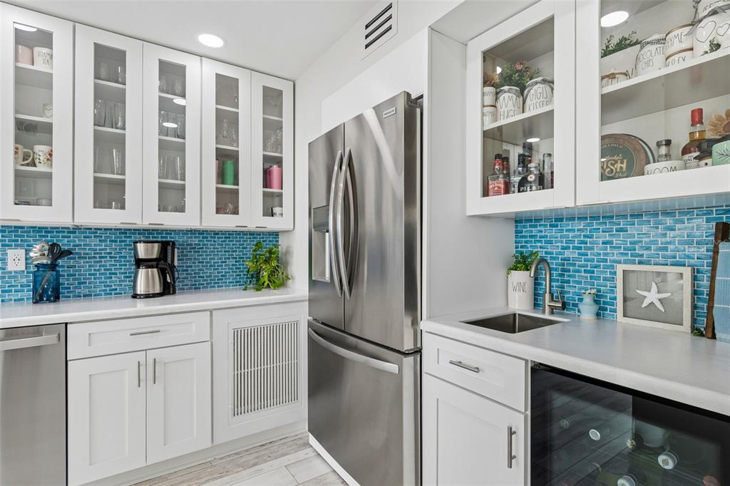 A kitchen features white cabinets, stainless steel appliances, and a blue glass tile backsplash — 644 ISLAND WAY UNIT 603, CLEARWATER BEACH, FL