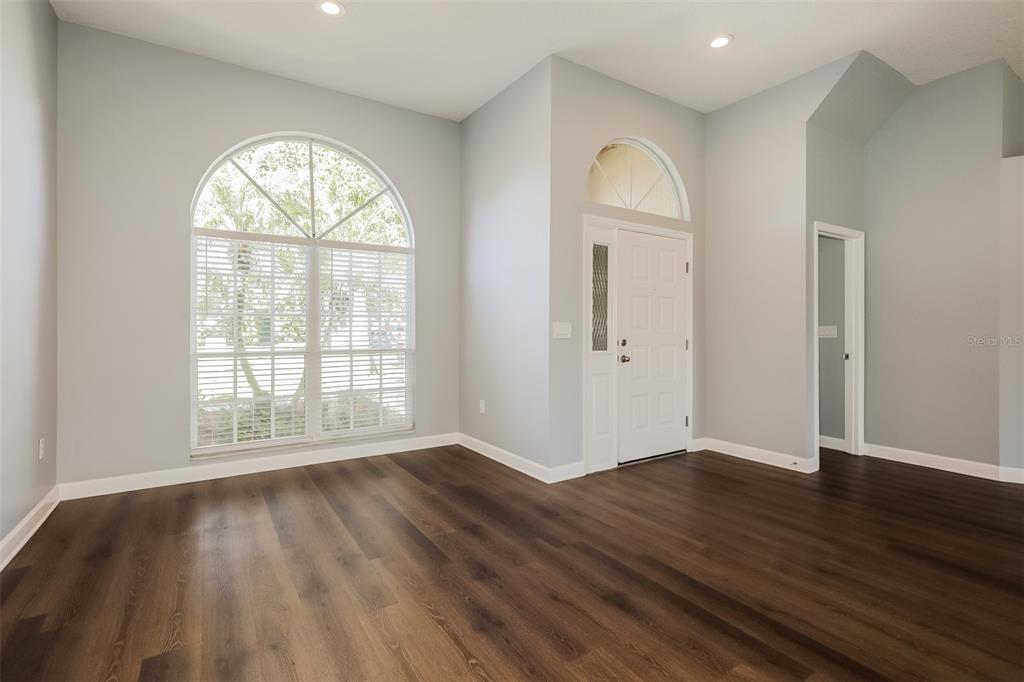 An empty room with dark wood-look flooring, light gray walls, and a large arched window — 5238 MONTSERRAT COURT, LAKELAND, FL