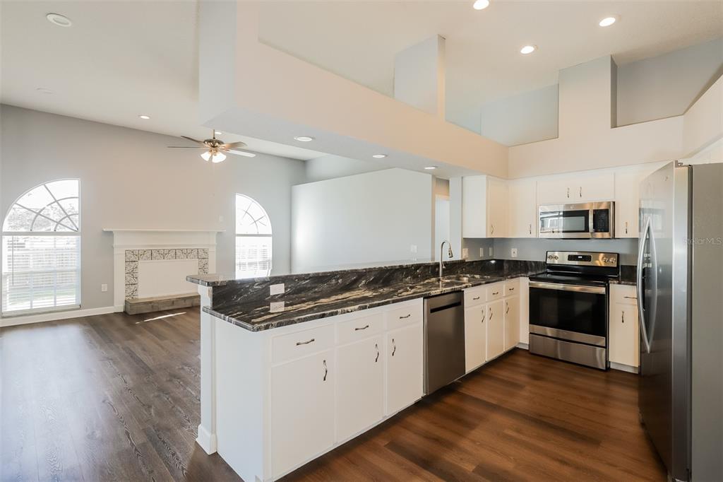 A kitchen with white cabinets and dark countertops overlooks a living room with a fireplace — 5238 MONTSERRAT COURT, LAKELAND, FL