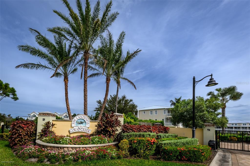 A stone monument sign for The Landings at Coral Creek stands before palm trees — 10300 TARPON LANDINGS TERRACE UNIT 4, PLACIDA, FL