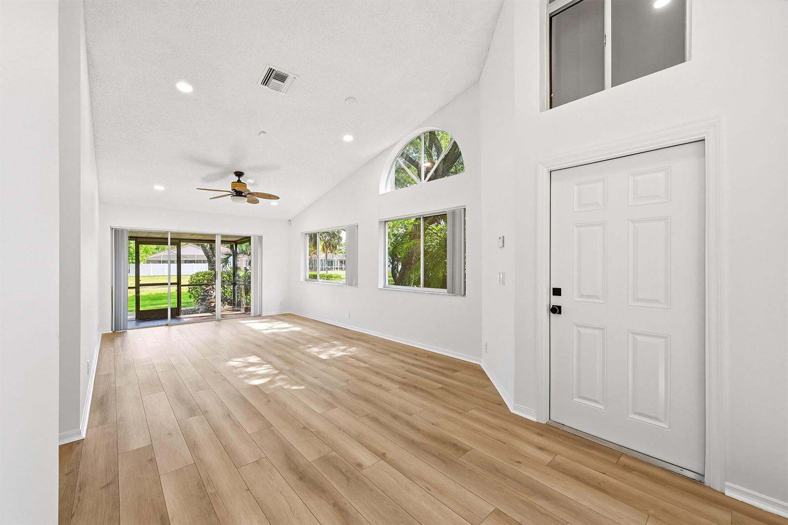 A bright, empty living room features vaulted ceilings, light wood flooring, and a glass sliding door — 7618 S Pinewalk Dr S # 132, Margate FL 33063, MARGATE, FL