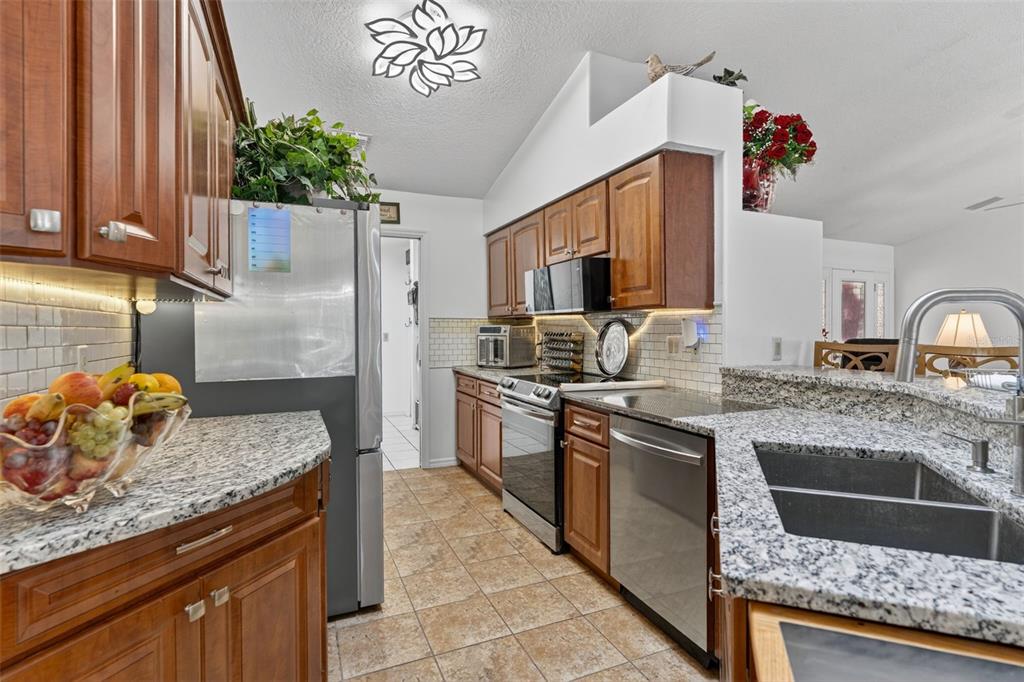A kitchen features wood cabinets, granite countertops, stainless steel appliances, and tile flooring — 507 E GILCHRIST COURT, HERNANDO, FL