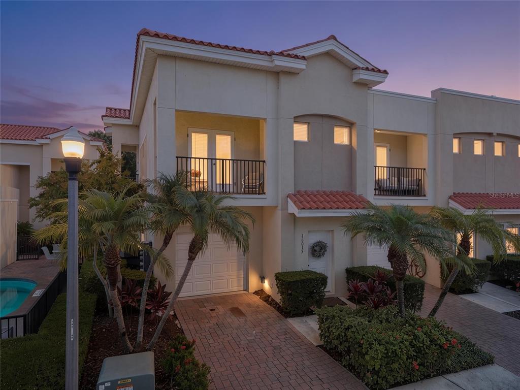 A two-story townhouse with a brick driveway, balconies, and palm trees at dusk — 10015 6TH STREET N, ST PETERSBURG, FL