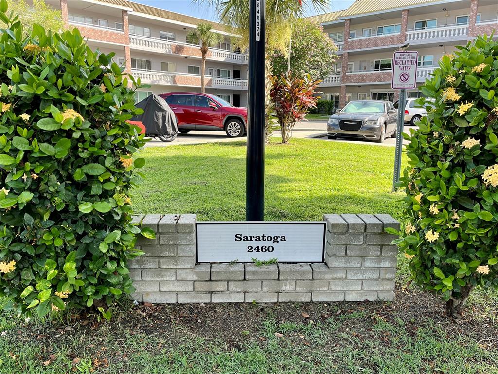 A brick sign for Saratoga 2460 stands in front of a multi-story apartment building — 2460 PERSIAN DRIVE UNIT 24, CLEARWATER, FL