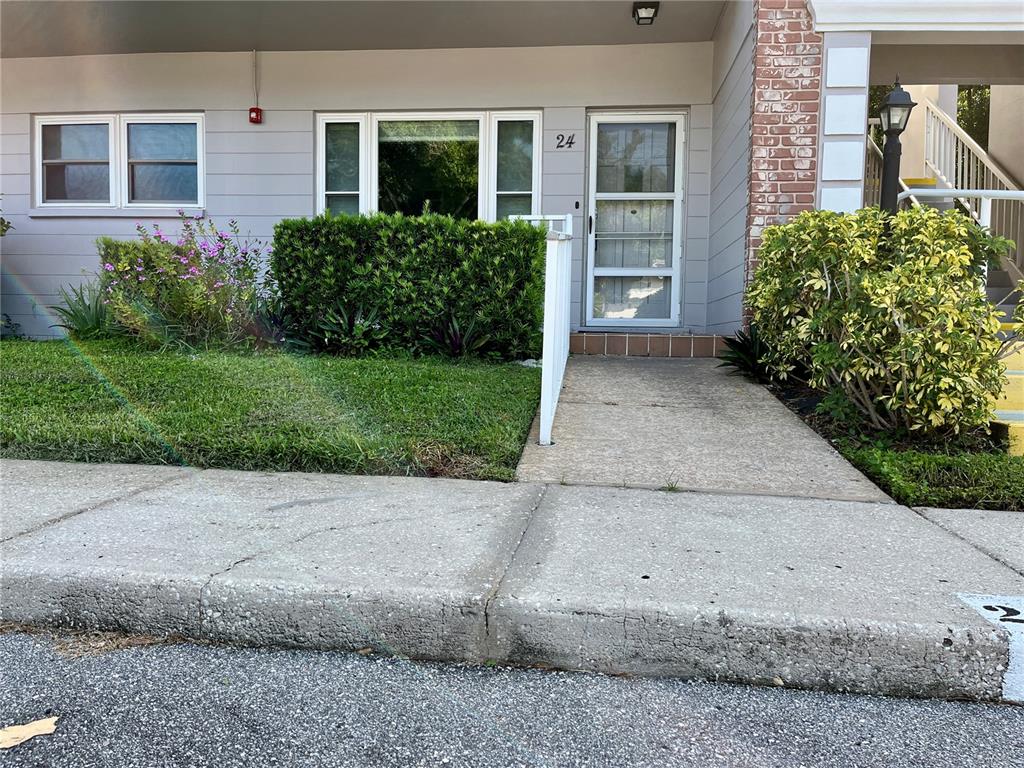 An exterior view of a ground-level apartment unit with a concrete walkway and landscaping — 2460 PERSIAN DRIVE UNIT 24, CLEARWATER, FL