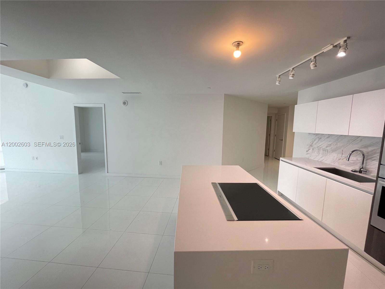 A modern kitchen features a white island with a cooktop and white cabinetry — 851 NE 1st Ave # 3103, Miami FL 33132, MIAMI, FL