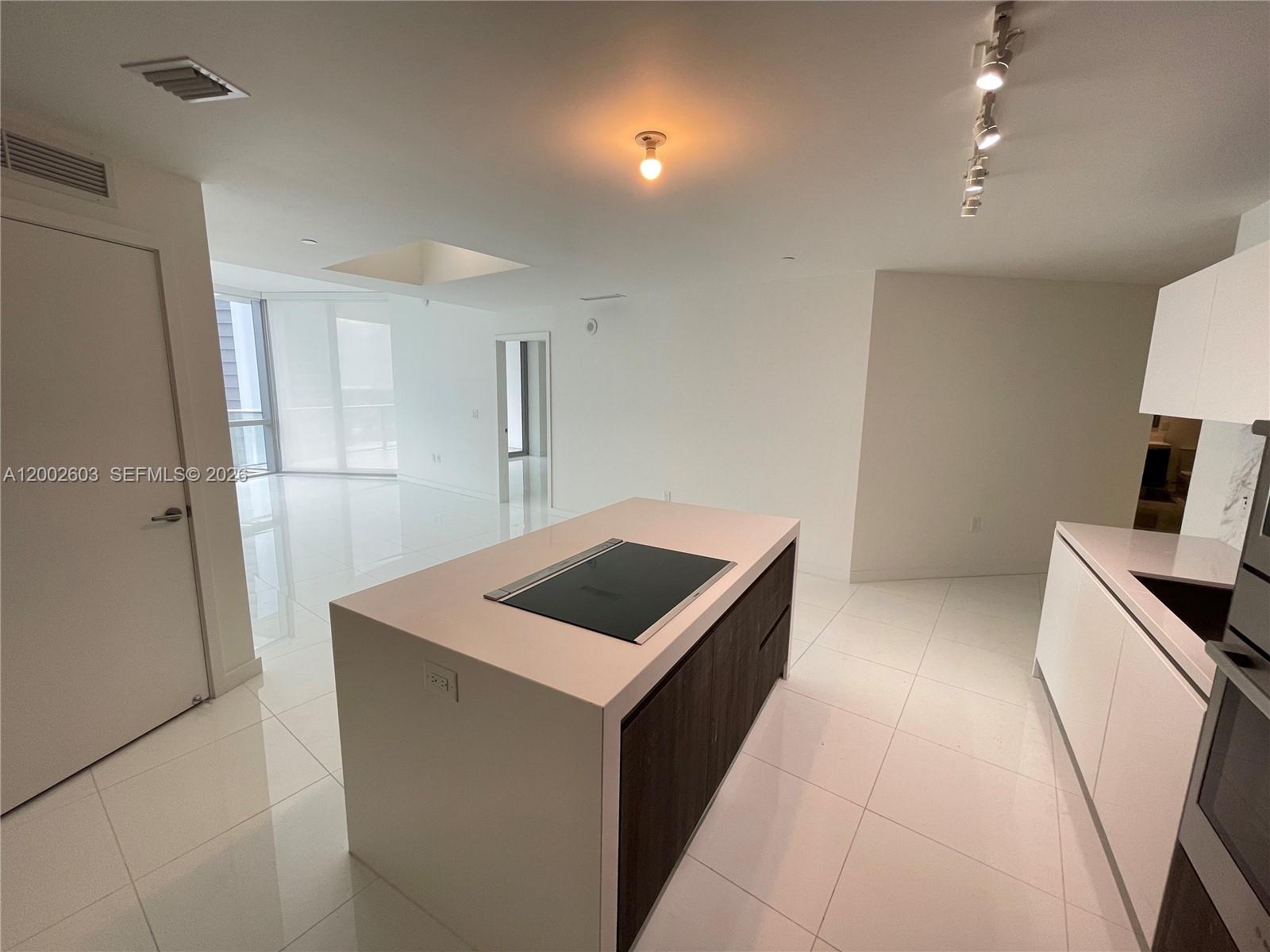 A modern kitchen features a central island with a cooktop, white cabinetry, and tile flooring — 851 NE 1st Ave # 3103, Miami FL 33132, MIAMI, FL