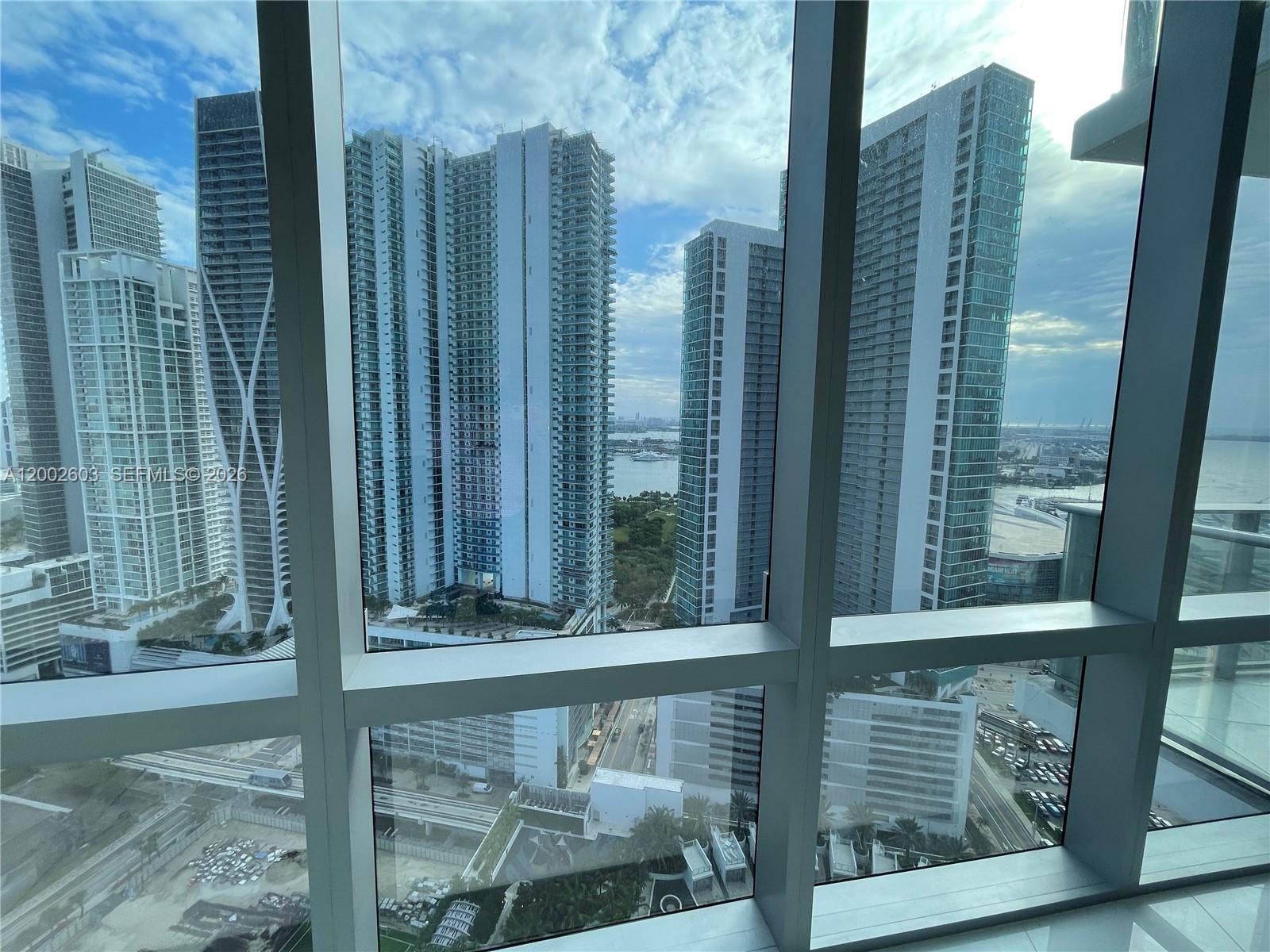 A high-rise view through floor-to-ceiling windows overlooking urban skyscrapers and a distant bay — 851 NE 1st Ave # 3103, Miami FL 33132, MIAMI, FL
