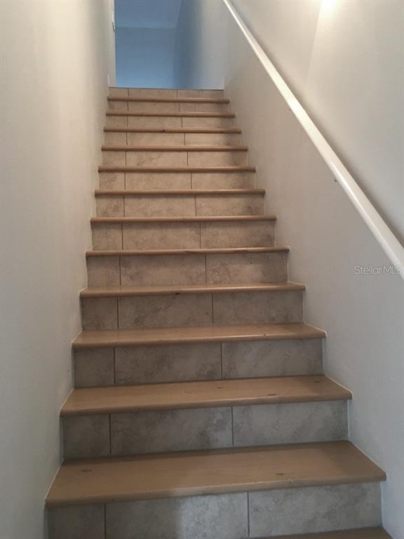 A straight staircase with tiled risers and wooden treads leads upward between two white walls — 6640 7TH AVENUE CIRCLE W UNIT 1513, BRADENTON, FL
