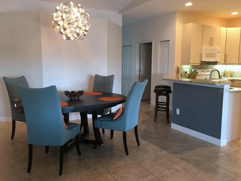 A dining area with a modern chandelier and blue chairs sits next to a kitchen — 6640 7TH AVENUE CIRCLE W UNIT 1513, BRADENTON, FL