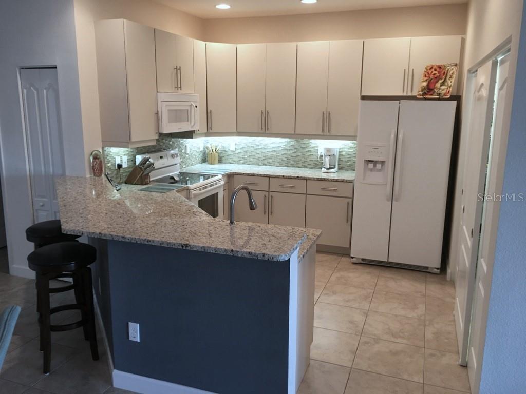 A kitchen with light-colored cabinets, granite countertops, a breakfast bar, and white appliances — 6640 7TH AVENUE CIRCLE W UNIT 1513, BRADENTON, FL