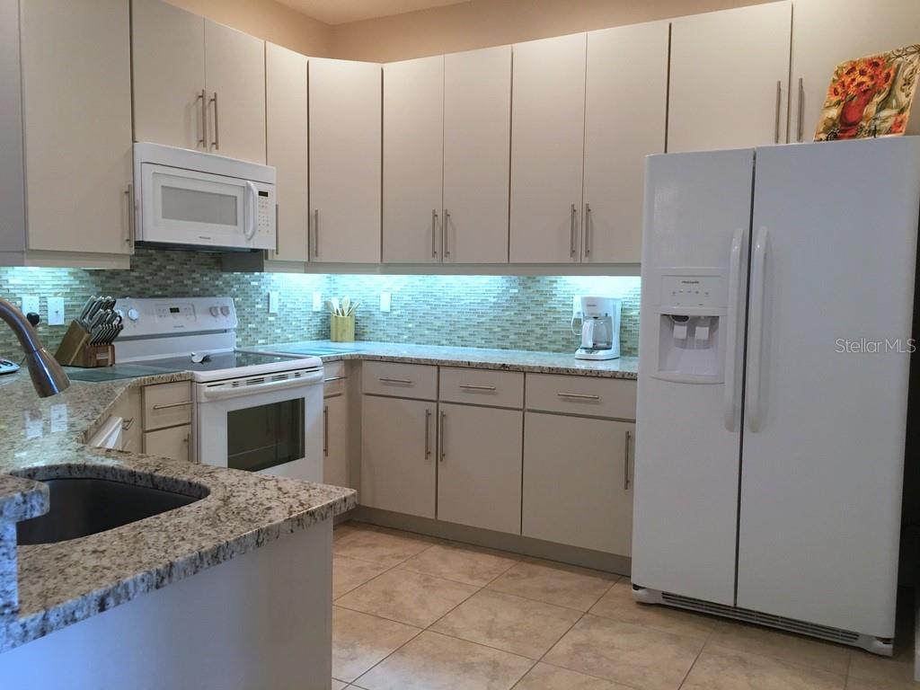 A kitchen with light-colored cabinets, granite countertops, white appliances, and a tiled backsplash — 6640 7TH AVENUE CIRCLE W UNIT 1513, BRADENTON, FL