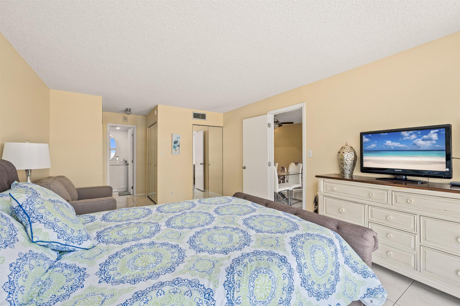 A bedroom features a bed with a patterned quilt, a dresser with a television, and tile flooring — 525 N Ocean Boulevard # 616, Pompano Beach FL 33062, POMPANO BEACH, FL