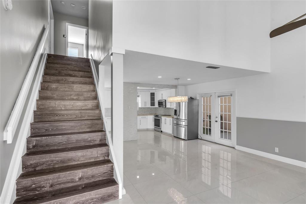 A staircase with wood-look treads leads to an upper level beside a tiled kitchen area — 4450 NW 55th Drive, Coconut Creek FL 33073, COCONUT CREEK, FL
