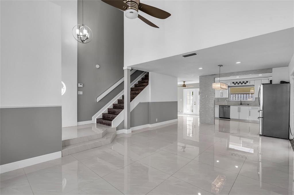 A bright open-concept living area features white tile floors, a staircase, and a modern kitchen — 4450 NW 55th Drive, Coconut Creek FL 33073, COCONUT CREEK, FL