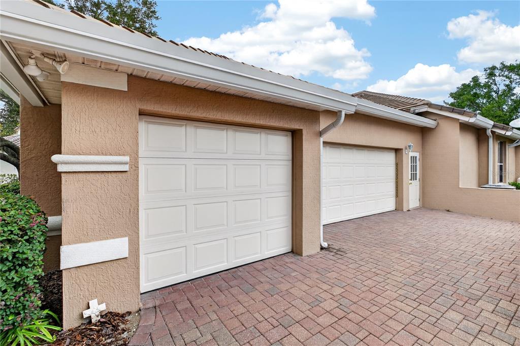 A tan stucco house exterior features two white garage doors and a brick paver driveway — 1911 BELFORD COURT, MAITLAND, FL