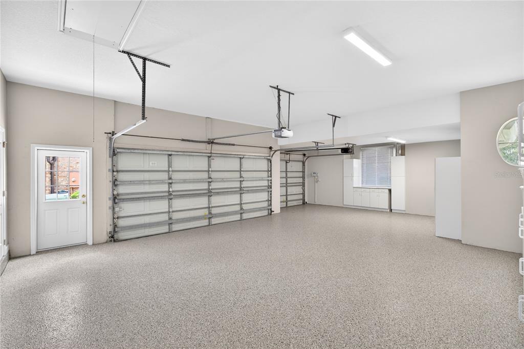 A spacious three-car garage features a speckled epoxy floor, white walls, and a side door — 1911 BELFORD COURT, MAITLAND, FL