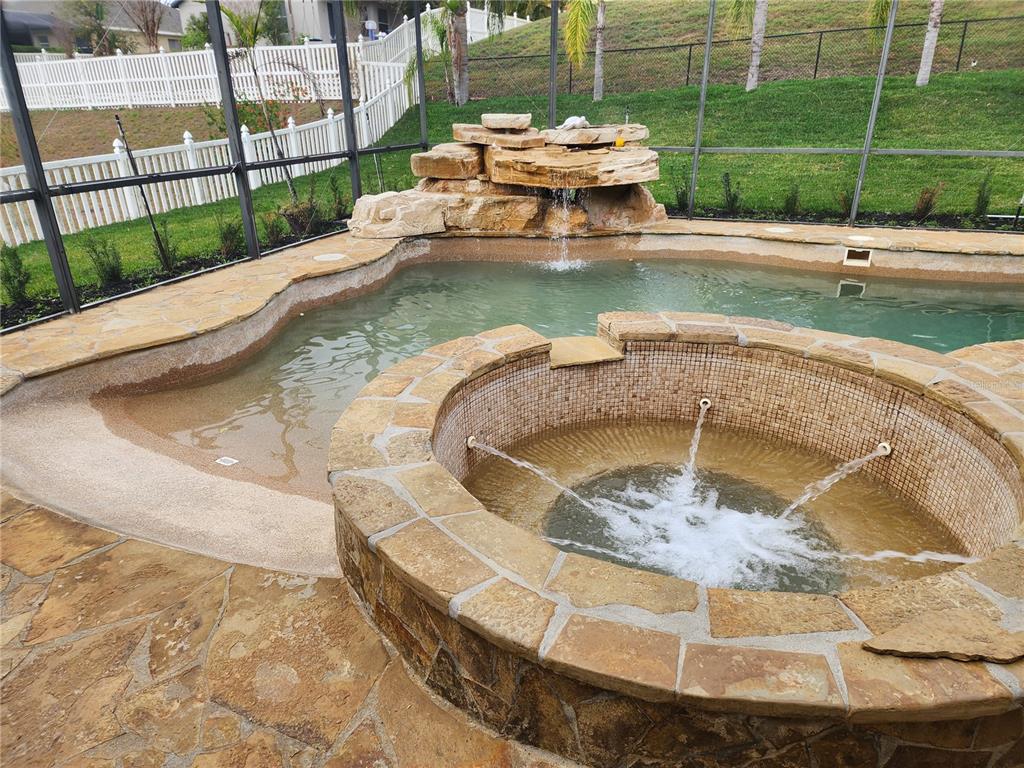 A backyard swimming pool with a stone waterfall and a circular tiled hot tub — 12027 STILL MEADOW DRIVE, CLERMONT, FL