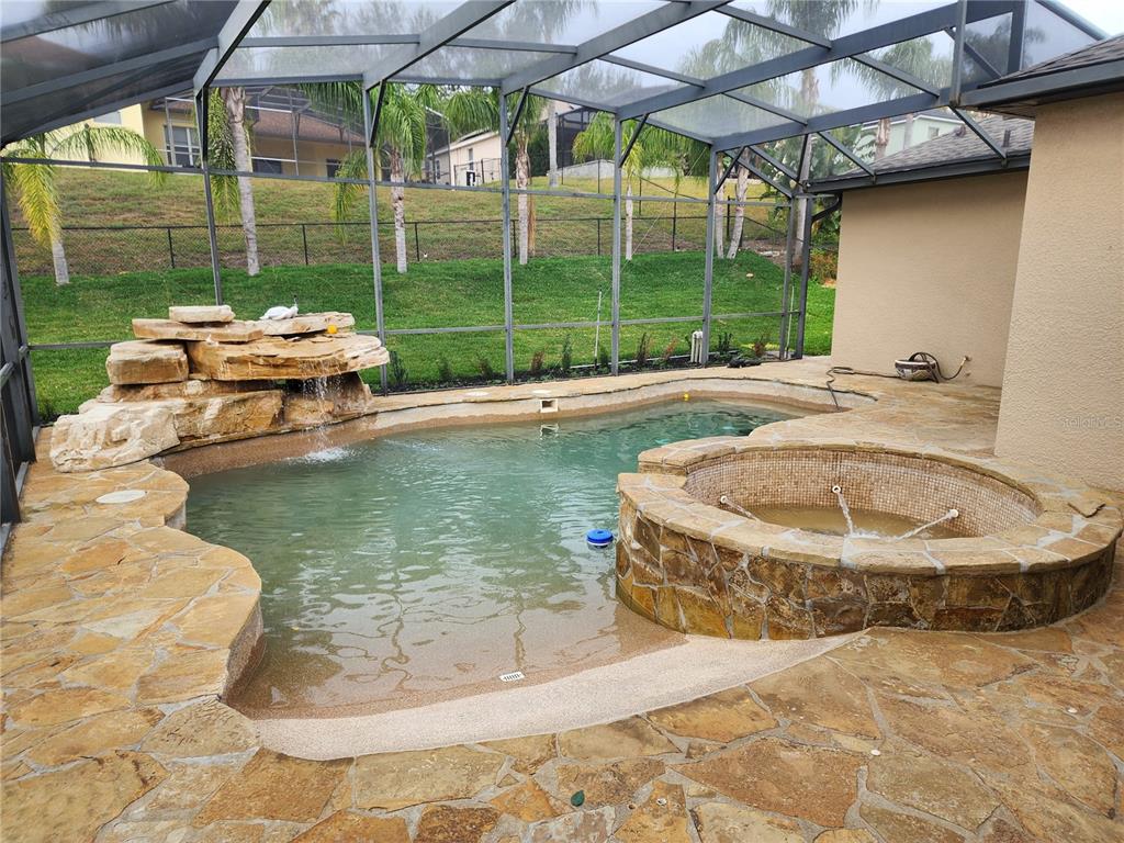 A screened-in pool area features a rock waterfall, a raised spa, and stone decking — 12027 STILL MEADOW DRIVE, CLERMONT, FL