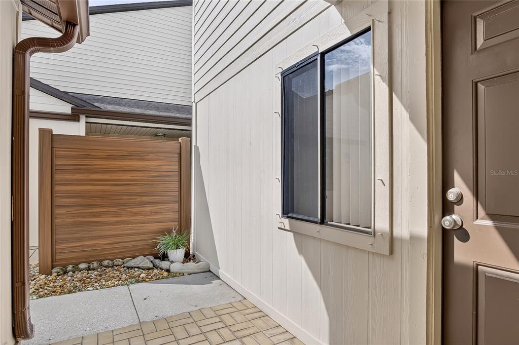 A brown door opens to a small patio with a wooden privacy fence and window — 367 CASTLEWOOD LANE, NEW SMYRNA BEACH, FL