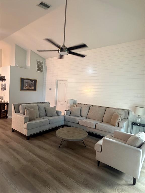 A living room features a vaulted ceiling, shiplap wall, ceiling fan, and light-colored furniture — 10467 LUCAYA DRIVE, TAMPA, FL