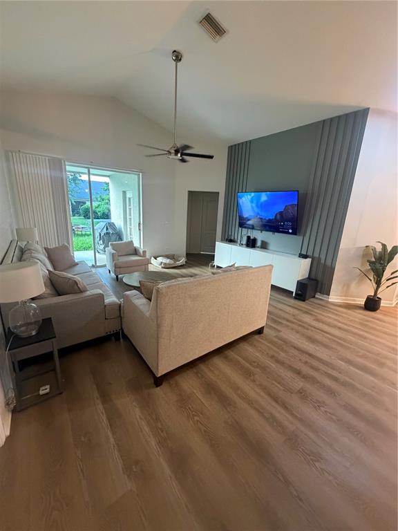 A living room features a vaulted ceiling, wood-look flooring, and a paneled accent wall — 10467 LUCAYA DRIVE, TAMPA, FL