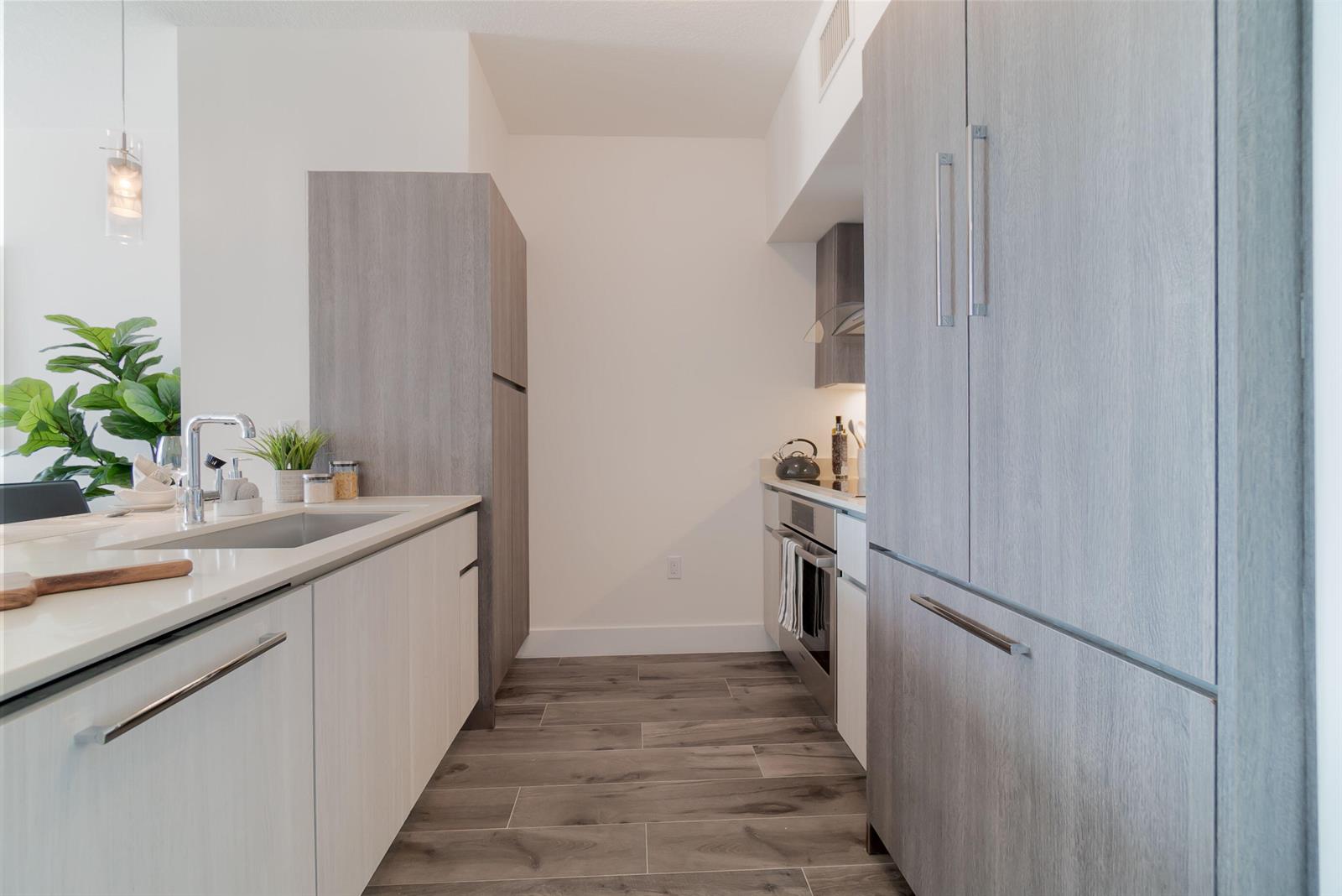 A modern kitchen features light wood cabinetry, white countertops, stainless steel appliances, and wood-look flooring — 111 SE 1st Avenue # 512, Delray Beach FL 33444, DELRAY BEACH, FL