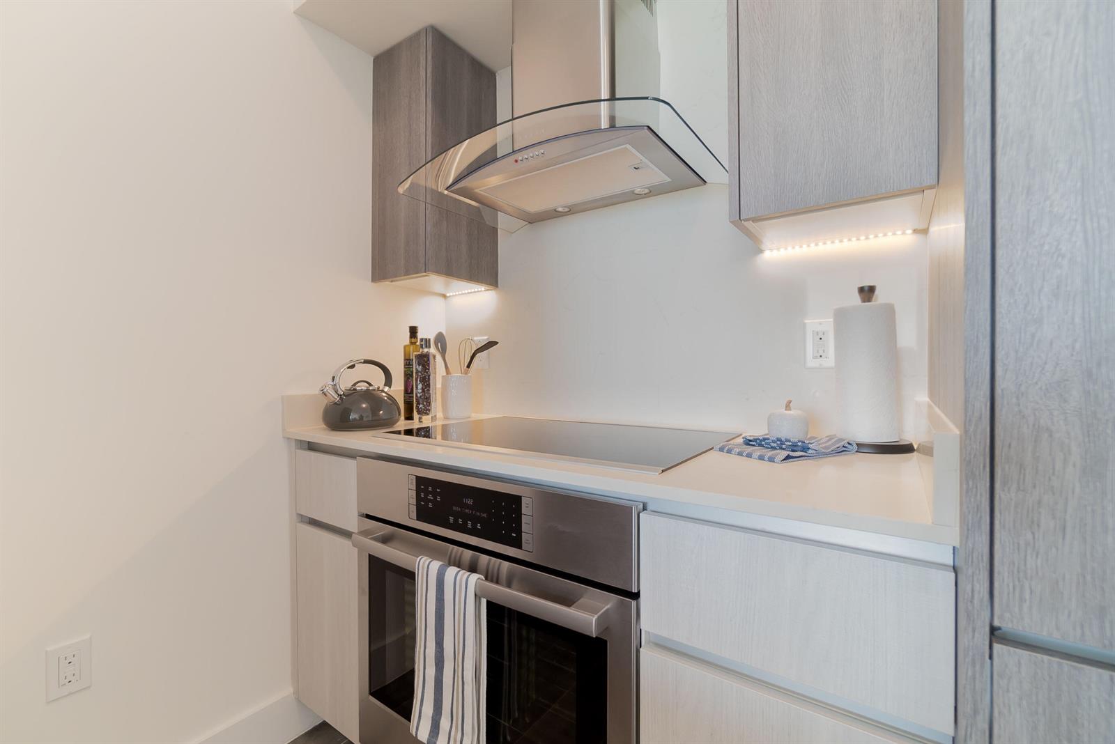 A modern kitchen features light wood cabinets, stainless steel appliances, and a glass range hood — 111 SE 1st Avenue # 512, Delray Beach FL 33444, DELRAY BEACH, FL