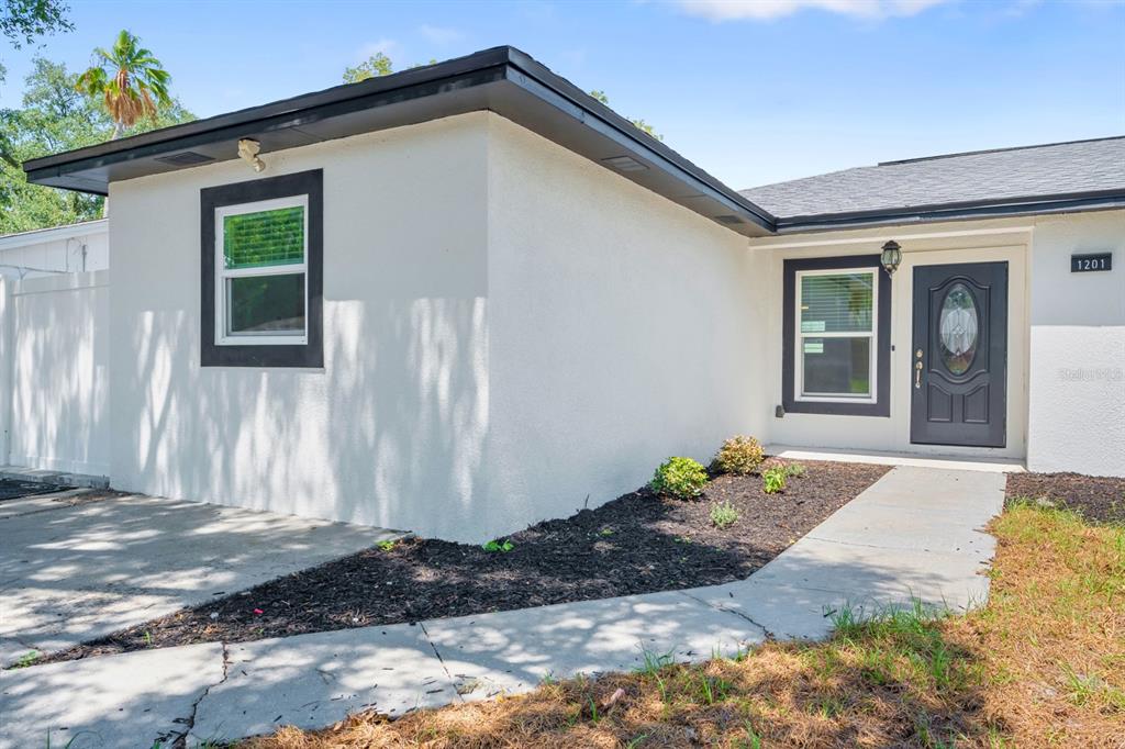 The exterior of a white stucco house features a dark front door and gray trim — 1201 WINDY RIDGE DRIVE, BRANDON, FL