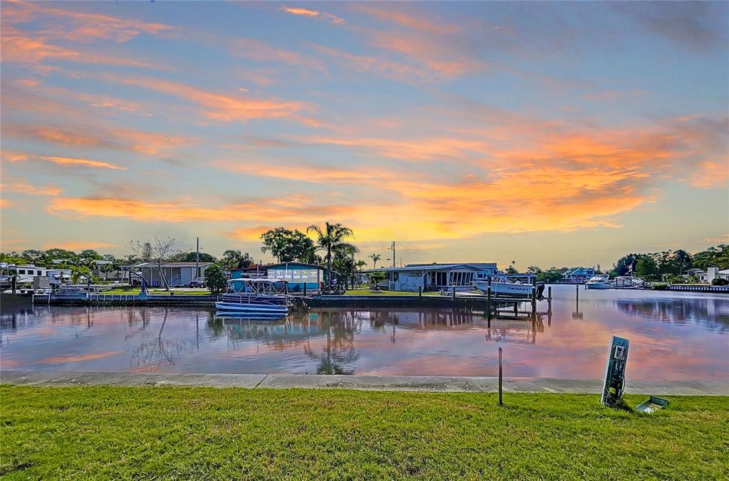 A waterfront view of a canal with docked boats under a vibrant sunset sky — 18 YAWL LANE UNIT 18, PALM HARBOR, FL