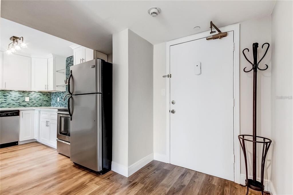 A kitchen with stainless steel appliances and white cabinets stands next to an entryway door — 51 ISLAND WAY UNIT 104, CLEARWATER BEACH, FL