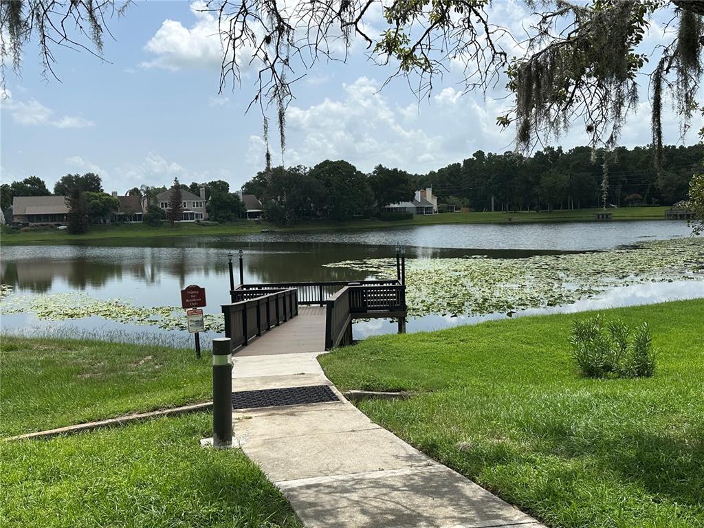 A concrete path leads to a wooden fishing pier extending into a pond with lily pads — 709 SECRET HARBOR LANE UNIT 101, LAKE MARY, FL