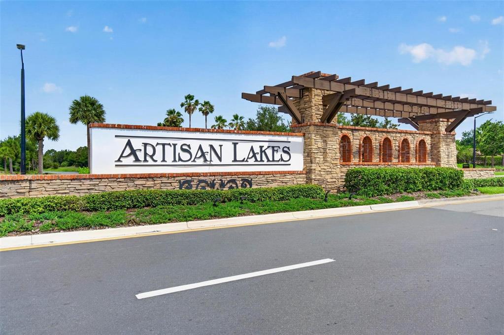 A stone monument sign for Artisan Lakes stands beside a road under a blue sky — 5636 MAIDENSTONE WAY, PALMETTO, FL