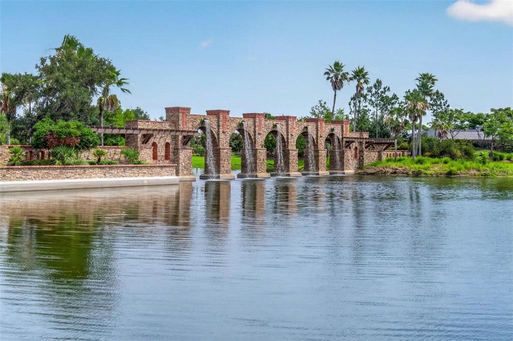 A stone aqueduct-style fountain with multiple water features stands in a lake near palm trees — 5636 MAIDENSTONE WAY, PALMETTO, FL