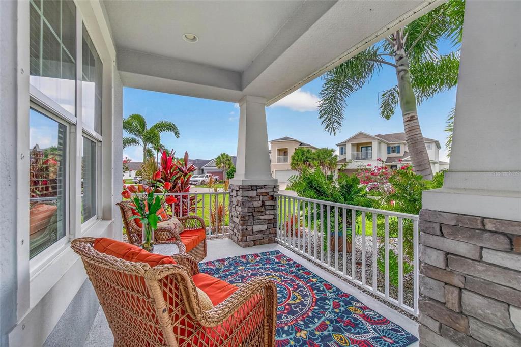 A covered front porch features two wicker chairs, a patterned rug, and stone-based columns — 5636 MAIDENSTONE WAY, PALMETTO, FL