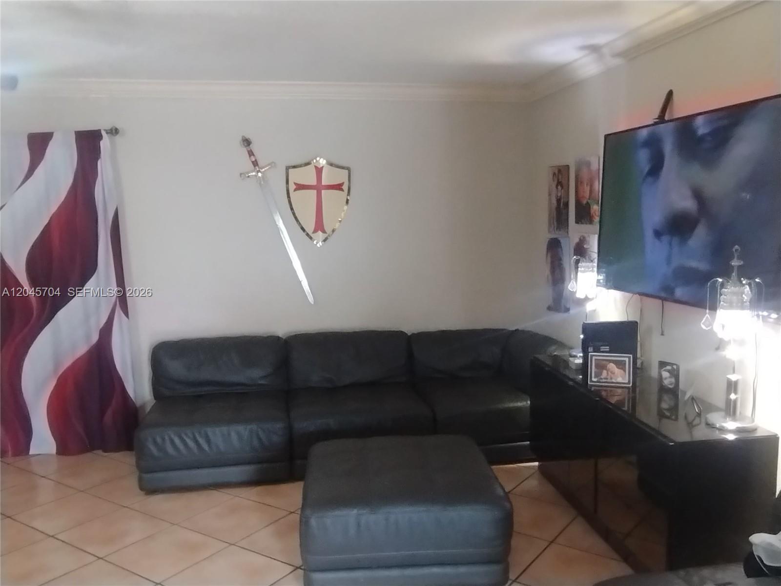 A living room features a black sectional sofa, a matching ottoman, and wall-mounted medieval decor — 7005 W 15th Ave, Hialeah FL 33014, HIALEAH, FL