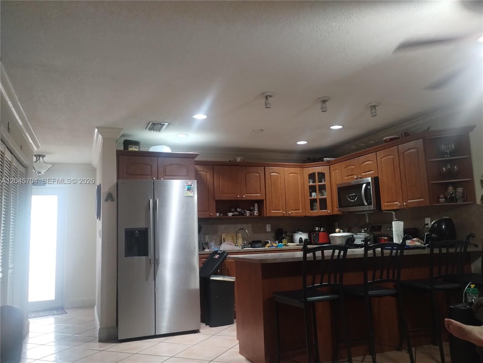 A kitchen features wood cabinets, stainless steel appliances, and a breakfast bar with stools — 7005 W 15th Ave, Hialeah FL 33014, HIALEAH, FL