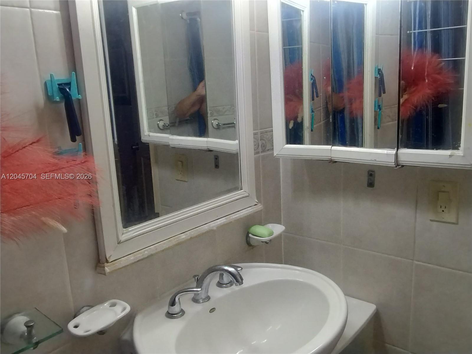A bathroom features a white pedestal sink, a wall-mounted medicine cabinet, and tiled walls — 7005 W 15th Ave, Hialeah FL 33014, HIALEAH, FL