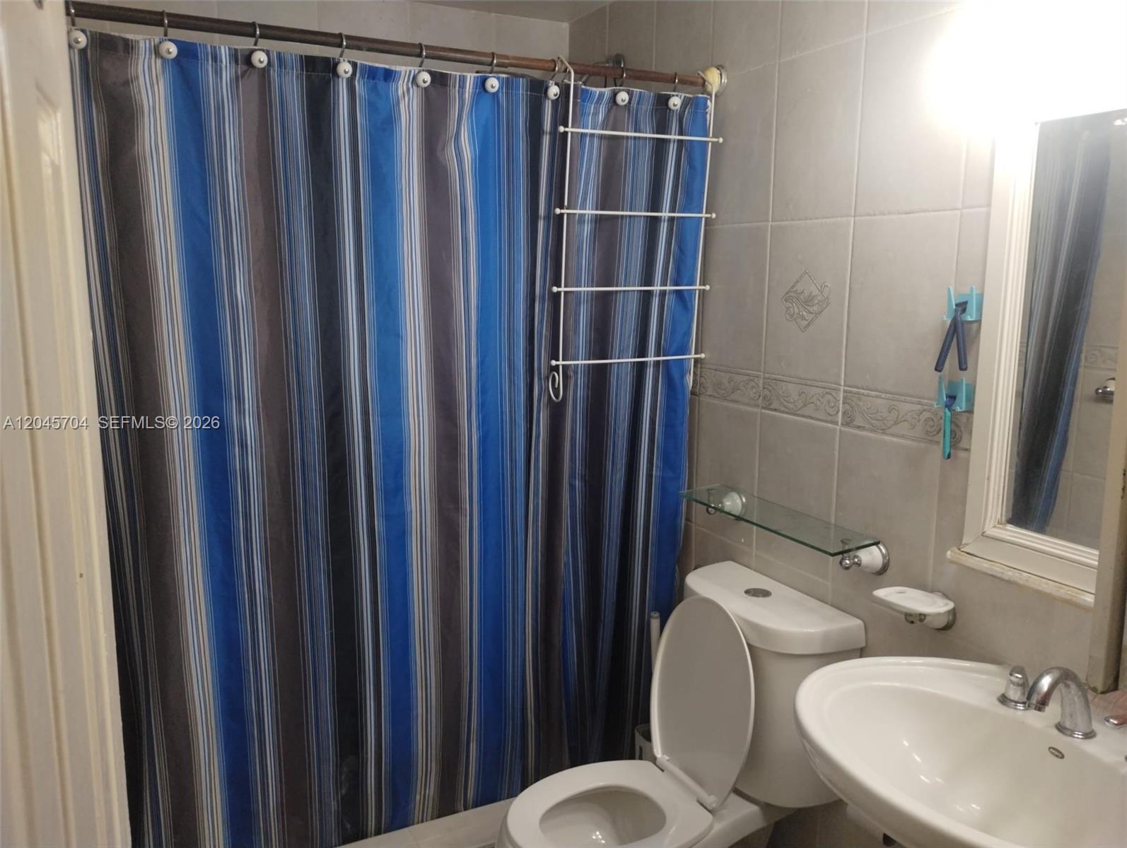 A bathroom features a blue striped shower curtain, a white toilet, and a pedestal sink — 7005 W 15th Ave, Hialeah FL 33014, HIALEAH, FL