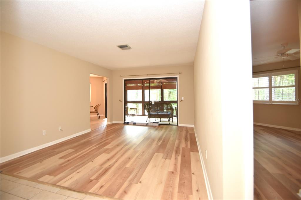A living room with wood-look flooring, beige walls, and sliding glass doors to a porch — 6 BROADMORE CIRCLE UNIT 6, PALM COAST, FL