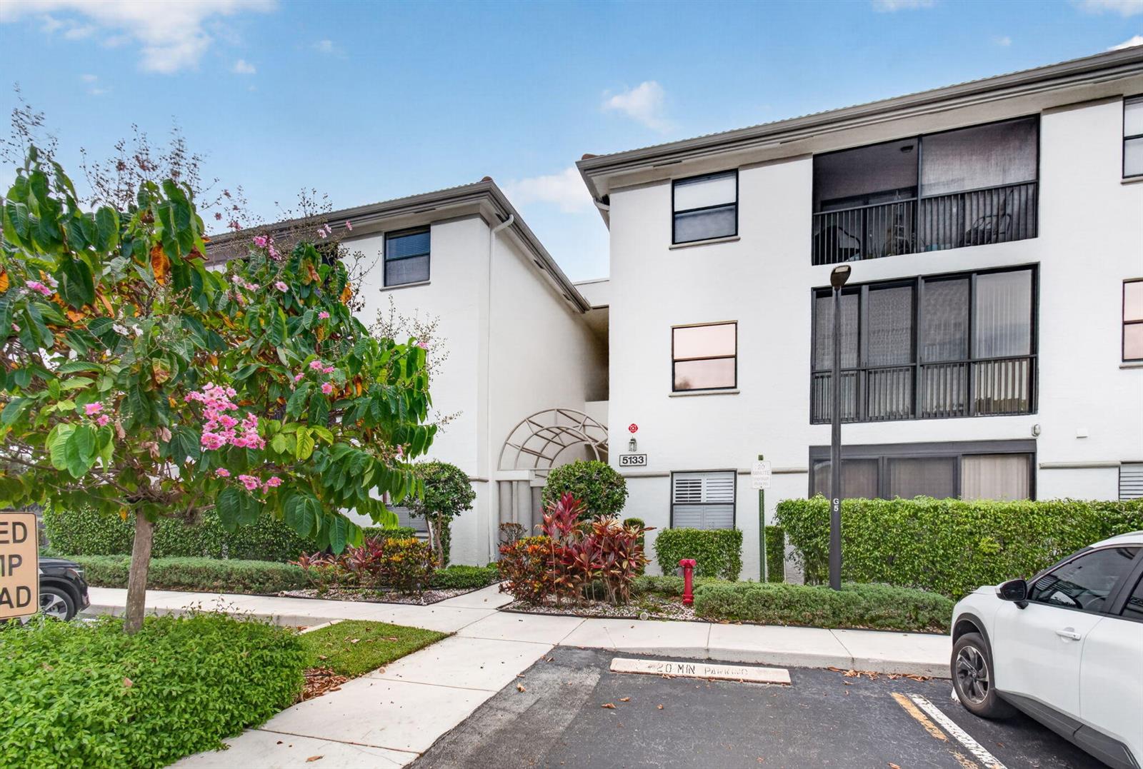 A three-story white apartment building features a landscaped entrance with a decorative metal archway — 5133 Brisata Circle # B, Boynton Beach FL 33437, BOYNTON BEACH, FL
