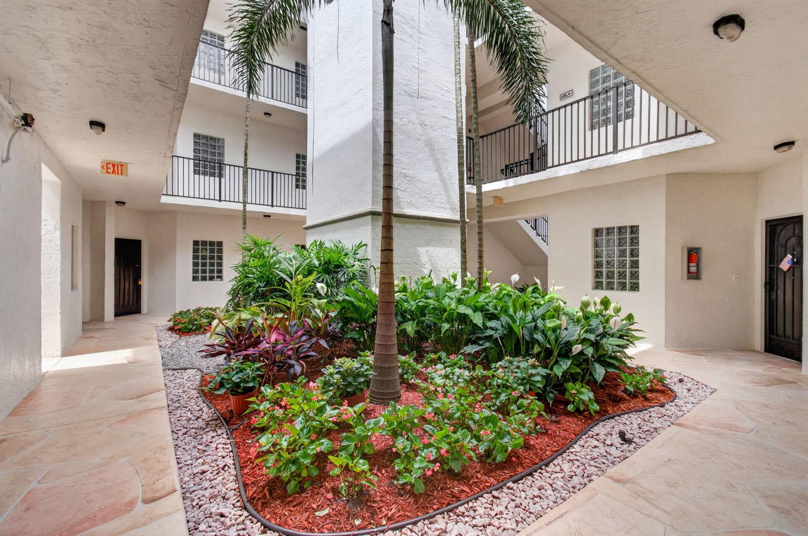 An open-air courtyard with a central garden bed, palm trees, and multi-level apartment balconies — 5133 Brisata Circle # B, Boynton Beach FL 33437, BOYNTON BEACH, FL