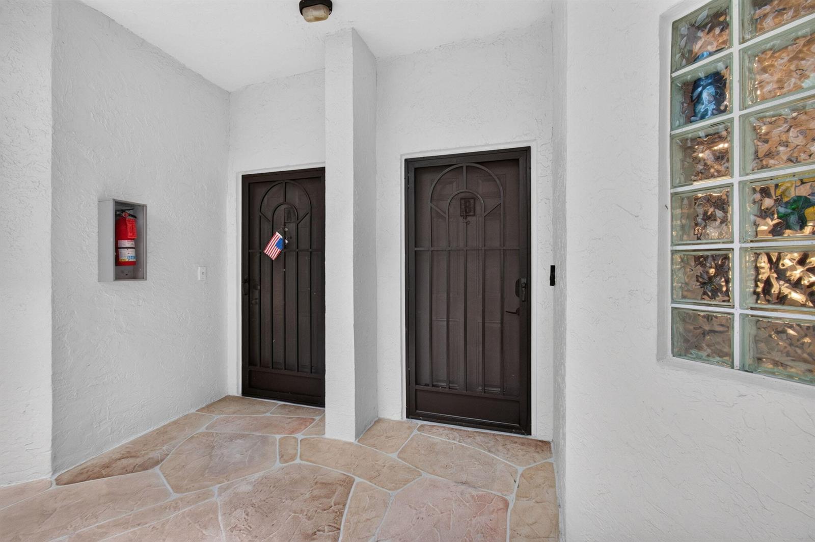 A covered entryway features two dark metal doors, a fire extinguisher, and stone-patterned flooring — 5133 Brisata Circle # B, Boynton Beach FL 33437, BOYNTON BEACH, FL