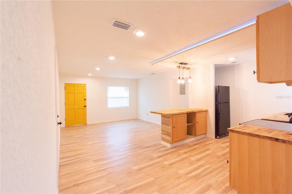 An open-concept kitchen and living area features light wood flooring and a yellow door — 6146 DAHLIA DRIVE, ORLANDO, FL