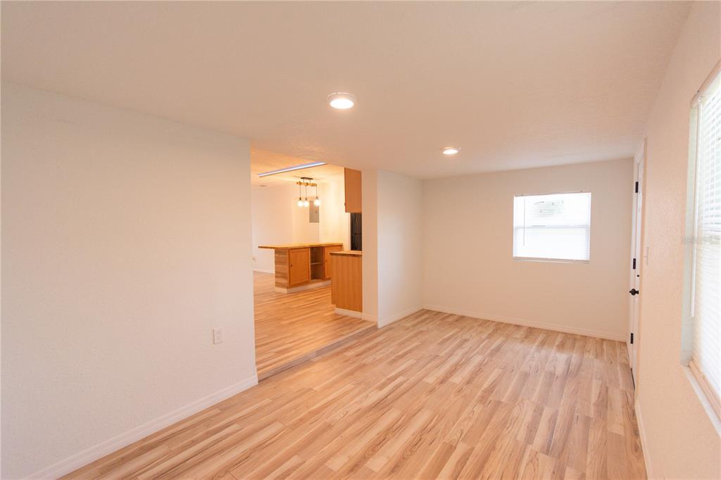 A living room with light wood-look flooring leads into a kitchen with wooden cabinets — 6146 DAHLIA DRIVE, ORLANDO, FL