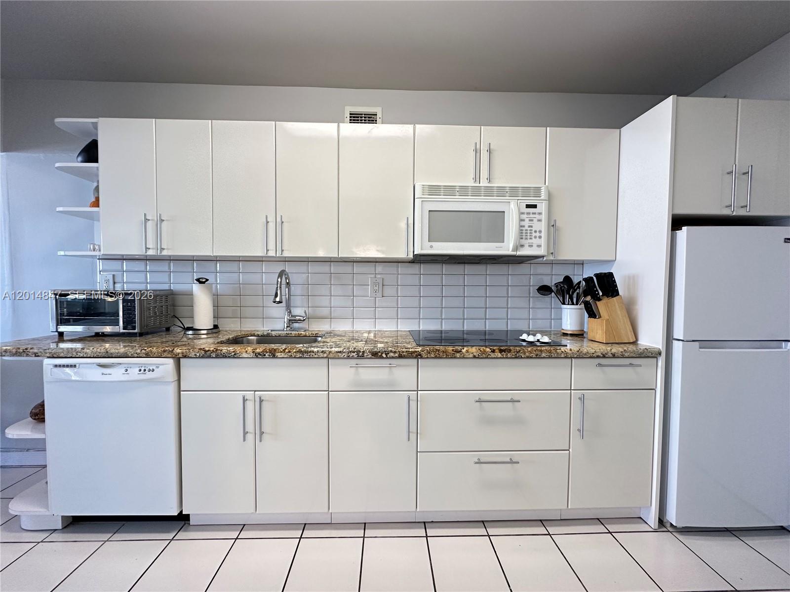 A kitchen features white cabinets, a granite countertop, a tiled backsplash, and white appliances — 100 Lincoln Rd # 1012, Miami Beach FL 33139, MIAMI BEACH, FL