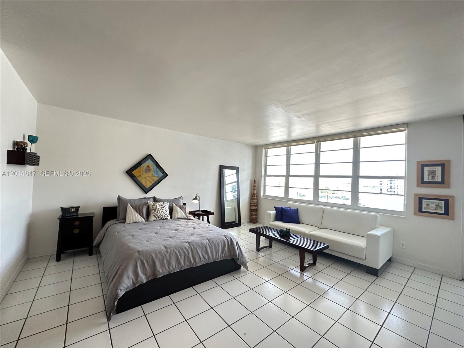 A bedroom with white tile floors, a bed, a white sofa, and large windows — 100 Lincoln Rd # 1012, Miami Beach FL 33139, MIAMI BEACH, FL